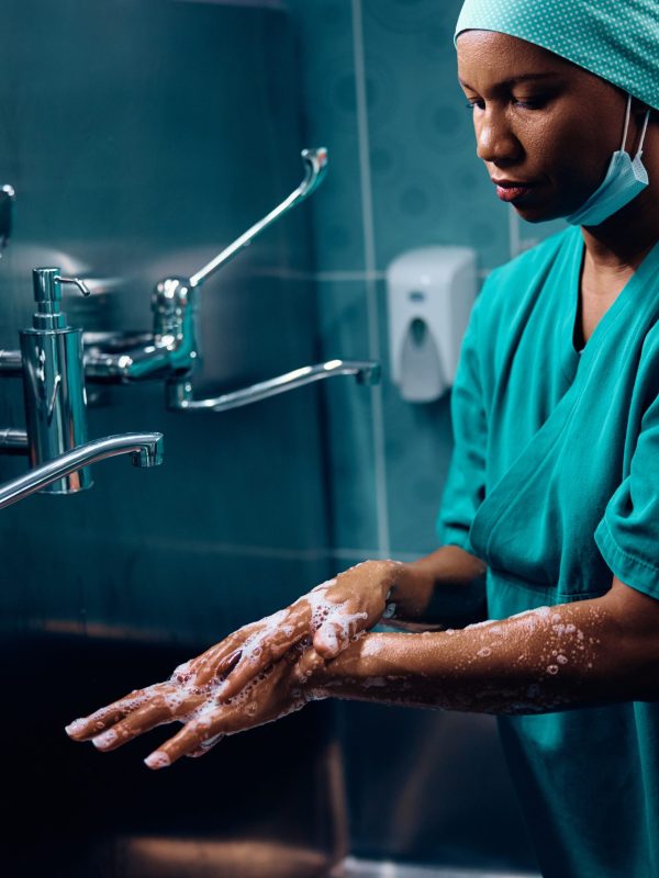 African American surgeon preparing for operating room while washing her hands at medical clinic. Copy space.